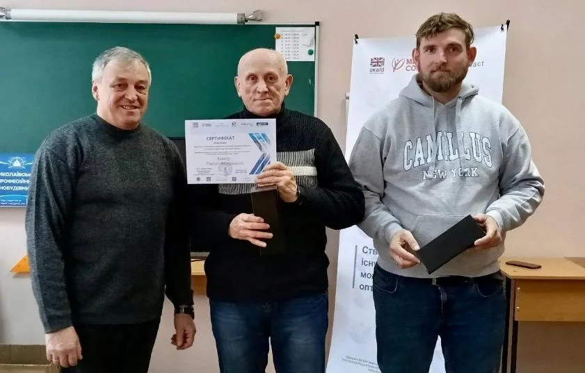 Сіміон (посередині) під час вручення сертифіката